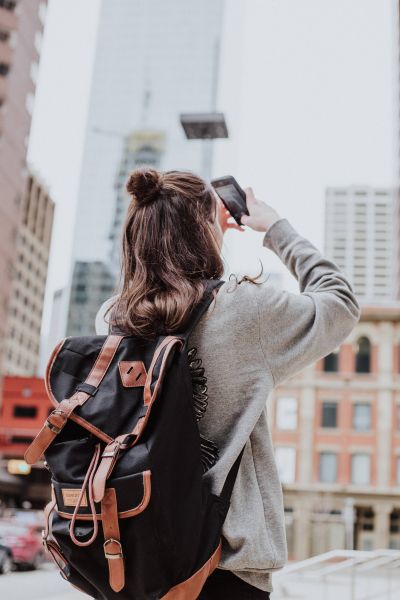 eine person mit rucksack fotografiert hochhäuser mit dem handy